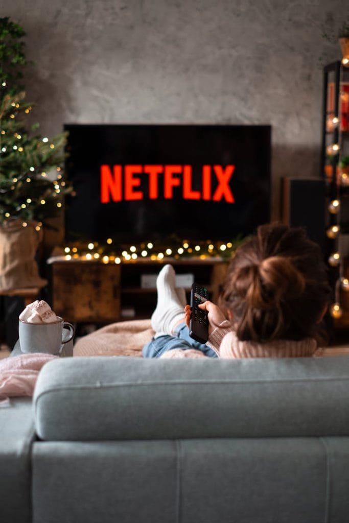 back-view-of-a-woman-sitting-on-a-sofa-and-watching-television-14756354 Woman relaxing on sofa with hot chocolate and Netflix on a winter evening.